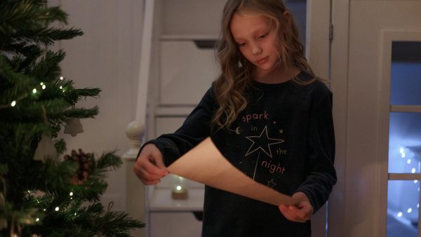 a young girl in black long sleeves reading a letter beside the christmas tree